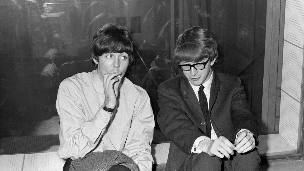 Paul McCartney smoking next to a man with glasses